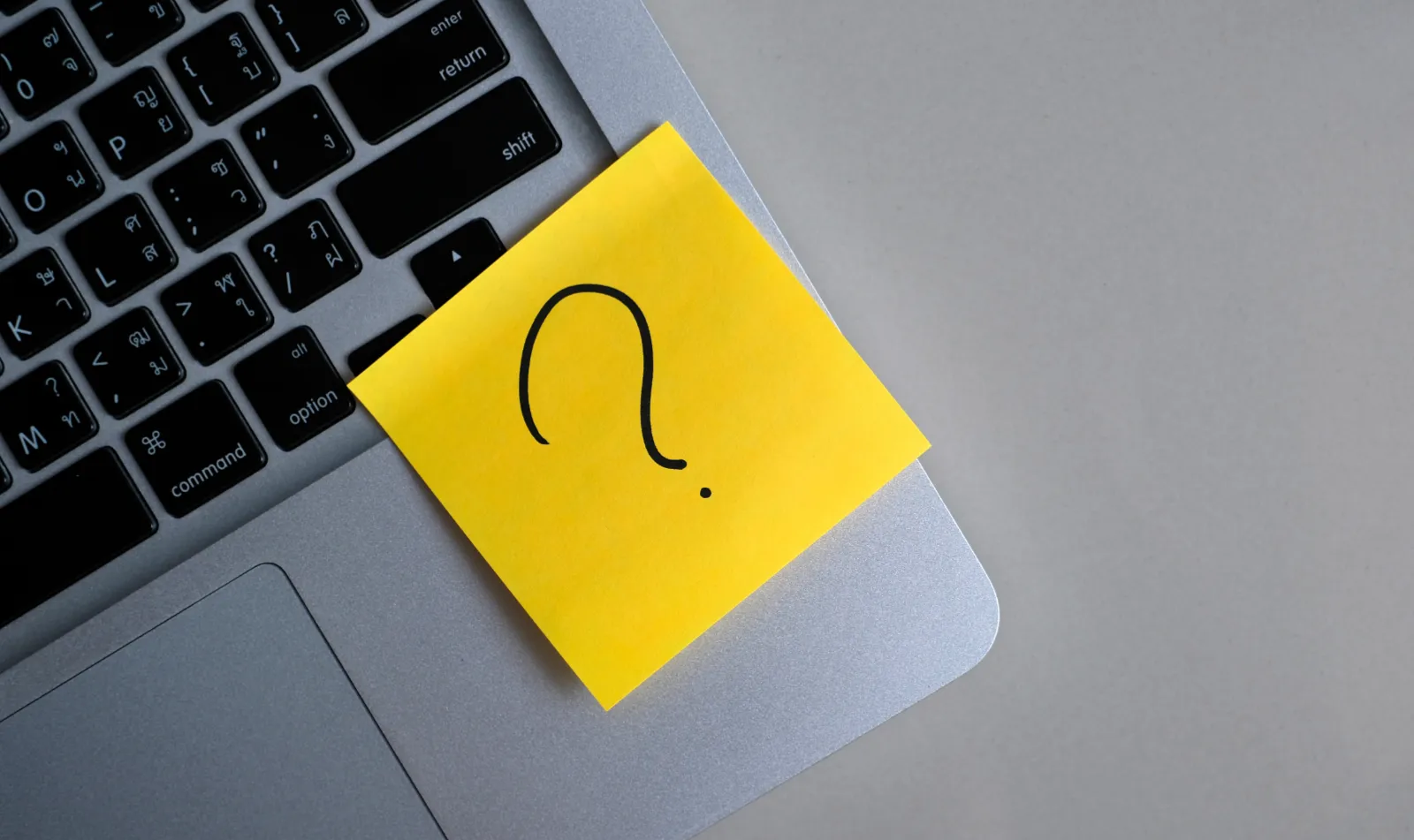 post-it jaune avec un point d'interrogation au feutre dessus posé sur le clavier d'un MacBook, vue aérienne pour illustrer Quel est le bon moment pour créer un site web pour son entreprise