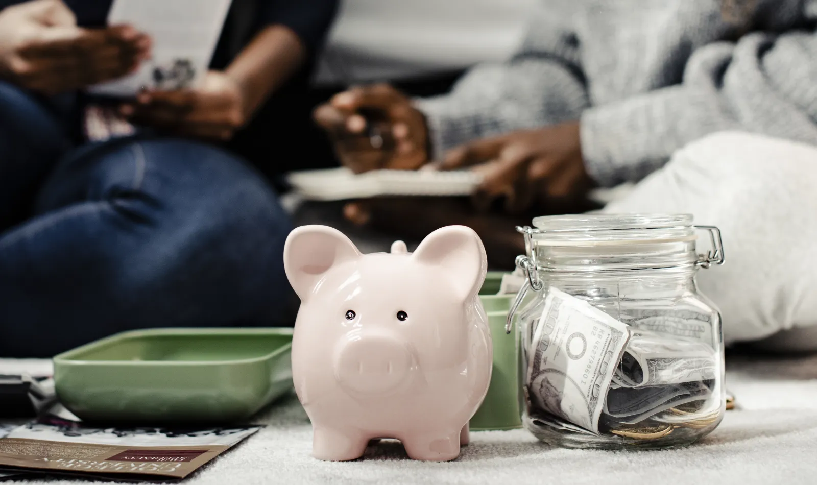 tirelire cochon en premier plan avec un bocal et de l'argent dedans et des personnes en fond pour illustrer le prix annueld 'un site web WordPress